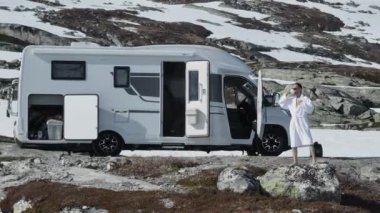 Beyaz bornozlu bir erkek gezgin muhteşem bir dağ kampında karavanının yanında sabah kahvesi içiyor. Manzaralı Norveç Manzarası.