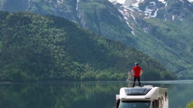 40 'lı yaşlarındaki Kafkasyalı Turist, karavanının çatısında kalırken Norveç manzarasının tadını çıkarıyor. Hava Görünümü.