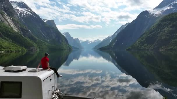 40代の白人男性がキャンパー ヴァンの屋根の上に座っている間にノルウェーの自然を楽しむ — ストック動画