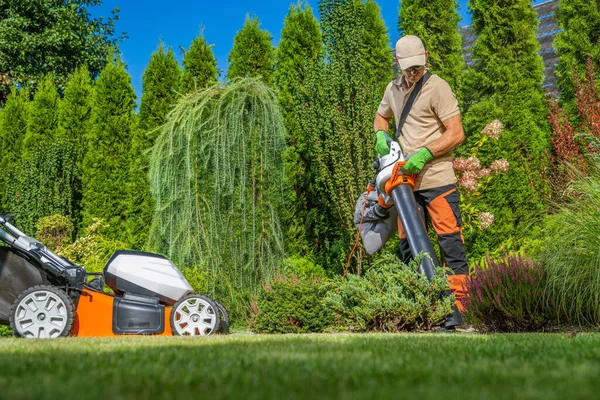 Backyard Owner with a Electric Garden Vacuum Cleaning His Yard. Lawn Maintenance.