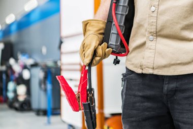 Ellerinde zıplama kablosu olan Oto Hizmet Merkezi İşçisi Aracı çalıştırmaya hazırlanıyor