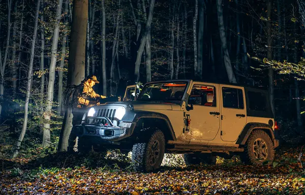 Emergency Missing Person Search in a Forest During Night Hours. Crew Member Looking on a Map While Standing Next to his AWD Vehicle.
