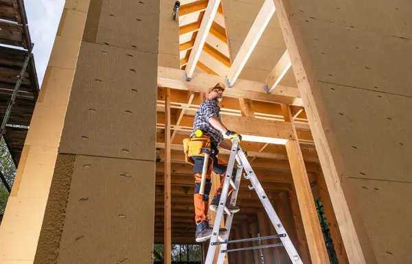 ラダーから天井ビームに到達するプロの建設請負業者労働者 ストック画像