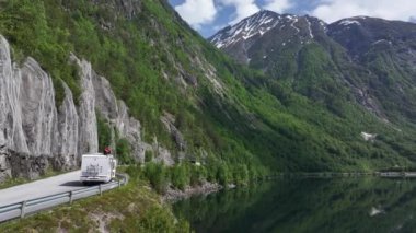 Mutlu Gezgin Dağ ve Alp Gölü Manzaralı Beyaz Kamp Arabasının Çatısında Rahatlıyor.