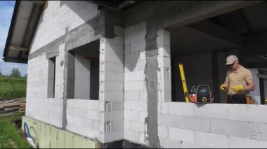 Bir adam beton bloklar kullanarak bir ev inşa ediyor. O kaldırıyor, istifliyor ve binanın duvarlarını inşa etmek için blokları düzenliyor. Bu süreç, sağlam bir yapı yaratmak için özenle çalıştığı için hassasiyet ve güç gerektiriyor..