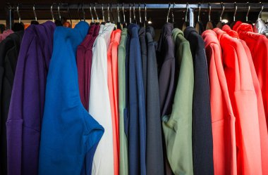 Canlı bir kapüşon çeşidi, müşterilerin bakması için çeşitli renkler ve stiller sergileyen bir perakende mağazasının rafında düzgünce asılı duruyor..