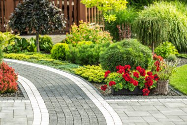 A beautifully landscaped garden features a winding stone pathway bordered by colorful flowers and greenery. clipart