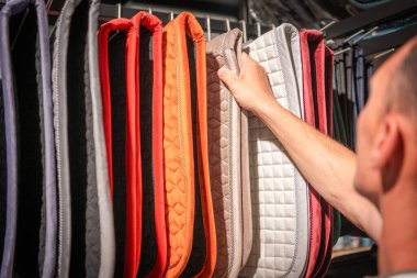 A hand reaches for a colorful assortment of saddle pads displayed in a tack shop, showcasing various textures and colors. clipart