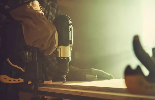 stock image A skilled craftsman operates a power drill on a wooden surface, illuminated by warm lighting, creating a focused atmosphere in the workshop.