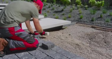 Bir işçi titiz bir şekilde zarif bir bahçeye kaldırımlar yerleştirir, güzel bir açık alanı titizlikle şekillendirir..