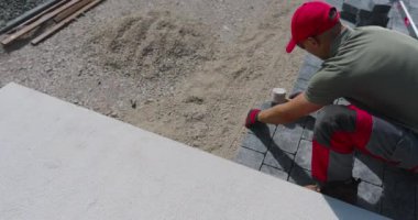 Bir işçi çakıl taşlarına titizlikle kaldırımlar yerleştirir, parlak güneş ışığında güzel bir bahçe alanı hazırlar..