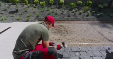 Bir işçi gün içinde çağdaş bir bahçe ortamında şık bir veranda oluşturmak için dikkatlice taşları yerleştirir..
