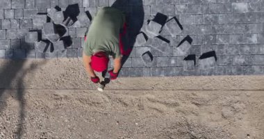 Bir işçi arka bahçede bir yürüyüş yolu yaratmak için kaldırım taşlarını dikkatlice döker. Proje üzerinde çalışırken güneş gölgeleri salıyor.