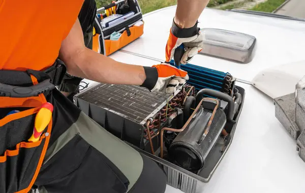 stock image A technician adjusts components of a rooftop RV Camper HVAC unit, using tools from an open toolbox, while working on a building.