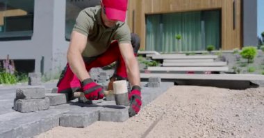 Bir kişi, modern bir açık alanda, hassasiyete odaklanarak bir geçit oluşturmak için taş bloklar yerleştiriyor..