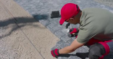 Bir işçi, taşları dikkatlice arka bahçeye serer. Her taşın hizalanmasını ve emniyette olmasını sağlar..