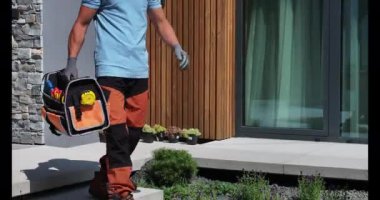 Bir adam, dış görevler için ekipman ve malzemelerle dolu bir alet çantası taşıyarak çağdaş bir evden çıkıyor..