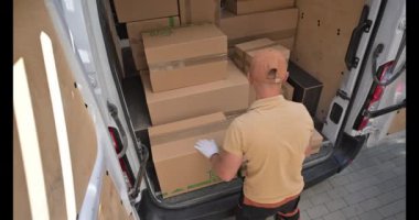 Teslimat işçisi, sakin bir mahallede park etmiş bir minibüsün karton kutularını dikkatlice boşaltıp dağıtıma hazırlanıyor..