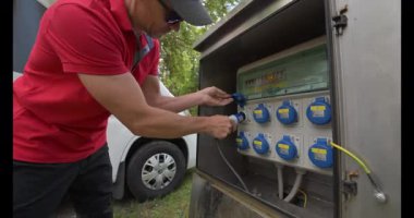 Bir insan yaz boyunca kampçılara elektrik sağlayan bir güç jeneratörünü bir kamp tesisine bağlıyor..