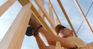 Bir inşaat işçisi ahşap kirişleri birleştirmeye odaklanır, parlak güneş ışığında marifetli bir işçilik sergiler..