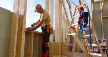 Becerikli bir marangoz, inşaat malzemeleriyle çevrili bir şekilde hassasiyet ve işçiliğe odaklanmış bir konutun içindeki yeni bir duvarı özenle çerçevelemeye çalışır..