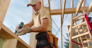 Yetenekli bir işçi ahşap kirişleri dikkatlice ölçer, bir evi çerçevelemeye hazırlanır. Açık öğleden sonra gökyüzü inşaat alanındaki verimli atmosfere ekleniyor..
