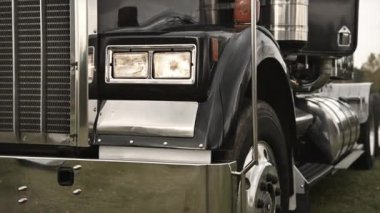 Klasik bir siyah kamyon, arka planda güneş batarken parlak krom ve sağlam tasarımını sergileyen bir otoyolun hemen yanında duruyor..