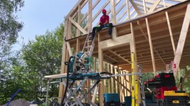 İnşaat işçileri ağaçların arasından güneş ışığı akarken ağaçların arasındaki merdivenleri ve elektrikli aletleri kullanarak ormandaki ahşap bir yapıyı çerçeveliyorlar..