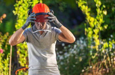 Güneşli bir günde bahçeyle uğraşmaya hazırlanırken kaskını ve yüz zırhını ayarlayan bir adam..