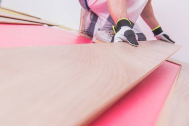 Bir işçi, iyi ışıklandırılmış bir alana ahşap döşeme döşeme döşeyerek, ev yenileme sürecinde dikkat ve hassasiyet sağlar..