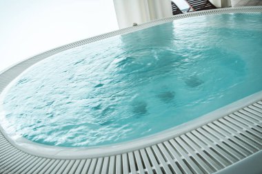 Berrak mavi suyla dolu sakin bir jakuzi, güneşli bir günde güzel bir okyanus manzarasına bakan rahatlamaya davetiye çıkarır..