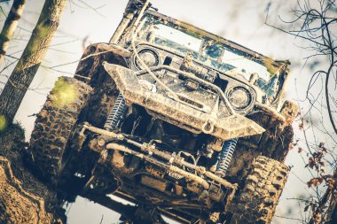 Yoğun bir ormanda çamurlu bir yokuşa çıkan bir arazi aracı engebeli tasarımını ve zorlu arazideki güçlü yeteneklerini sergiliyor..