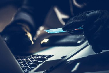 Eldivenli bir kişi dizüstü bilgisayarın başındayken kredi kartı bilgilerini çalmaya çalışıyor. Çevre karanlık, yasadışı faaliyet olduğunu gösteriyor..