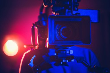 Bir film yapımcısı, renkli ışıklar stüdyoyu aydınlatırken profesyonel bir kamera kurar ve çekim için dinamik bir atmosfer yaratır..