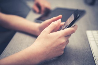 Bir kişi akıllı telefonuyla meşgul olur, yanında tablet ve klavyeyle bir masada otururken konsantre olur ve verimli bir ortam yaratır..