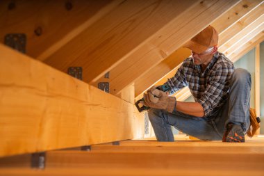 Bir marangoz çatı katında ahşap kirişleri güvence altına almaya ve yenileme projesi sırasında yapısal istikrarı sağlamaya odaklanır..