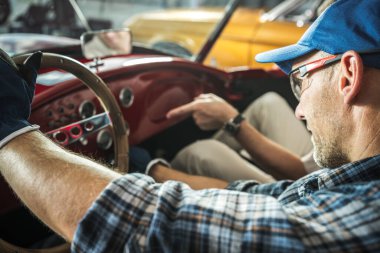 Bir araba meraklısı garajda antika bir araba üzerinde çalışırken gösterge paneli parçalarını inceler. Atmosfer otomobil restorasyonuna olan tutkuyu ortaya çıkarıyor..