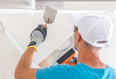 Mavi gömlekli ve eldivenli bir adam alçıpan tamir eder. Bir mala kullanarak yüzeyi düzleştirmeye odaklanır. İyi aydınlatılmış, çağdaş bir ortamda..