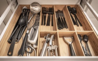 Düzenli bir mutfak çekmecesinde çırpı ve çatal bıçak gibi çeşitli mutfak aletleri kullanıma uygun bölmeler halinde düzenli olarak sergilenir..