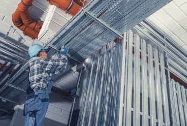 Bir inşaat işçisi, yeni bir binada yapısal istikrarı sağlamak için, yukarıda metal iskelet kurmaya odaklanmış durumda. Çevre endüstriyel ve aktiftir.