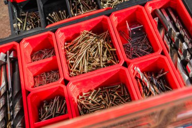 Çeşitli vida ve matkap uçları, ev geliştirme veya inşaat projeleri için ideal kırmızı bir alet kutusunun bölümlerinde düzenli olarak düzenlenir.