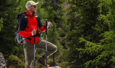 Yürüyüşçü, güneşli bir günde, bereketli ağaçlarla çevrili bir dağ yolundaki güzel çevrenin tadını çıkarmak için durur. Doğanın huzurunun tadını çıkarır..