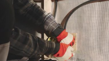 Bir birey elektrik bağlantıları hazırlıyor, eldiven takıyor ve yeni inşa edilmiş bir yapının içindeki kabloları güvenli bir şekilde bağlamaya odaklanıyor. Malzemeleri dikkatle taşıdıkları için tedbirler açıkça ortada..