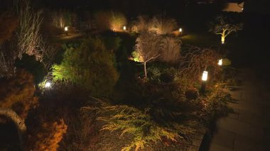 Güzelce döşenmiş bahçe, gece gökyüzünün altındaki fenerlerle hafifçe aydınlatılır. Ağaçlar ve çalılar dinlenmek için mükemmel bir ortam yaratıyor..