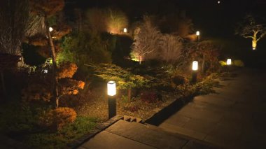 Gün batımından sonra güzel ışıklandırılmış bir bahçede dolaşmak, yemyeşil bitkiler, sanatsal peyzaj ve sakin atmosferi geliştiren sakinleştirici ışık..