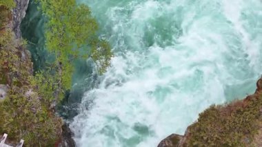 Çarpıcı bir manzara, canlı yeşillik ve çarpıcı mavi sularla çevrili kayalık bir arazide çağlayan güçlü bir nehri yakalar. Doğanın güzelliği gözler önünde..