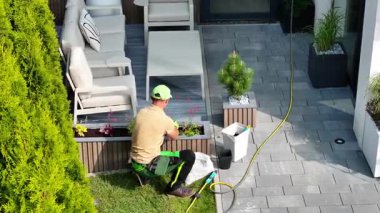 Bir bahçıvan titizlikle çiçek dikmeye ve şık bir avluda yeşillik düzenlemeye çalışır. Kurulumda çağdaş mobilyalar ve iyi bakımlı taş yollar yer alıyor..