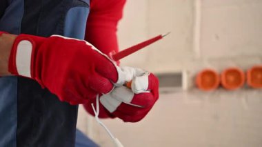 Yoğun bir atölyede, koruyucu eldivenler giymiş yetenekli bir elektrikçi çeşitli onarım işleri için gerekli alet ve malzemeleri titizlikle hazırlar, güvenlik ve hassasiyeti sağlar..