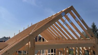 İşçiler sağlam ahşap bir çatı inşa ediyorlar. Parlak mavi gökyüzü projenin ilerlemesini vurguluyor, zanaat ve beceri sergiliyor.