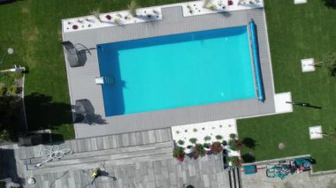 Parlak ve davetkar bir yüzme havuzu güzel manzaralı bir arka bahçede oturur. Her şeyin pırıl pırıl olmasını sağlamak için bakım çalışmaları devam ederken yemyeşil havuzu çerçeveler..